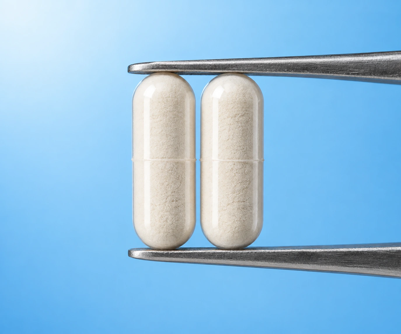 Two clear powder-filled capsules held between metal tweezers against a blue background